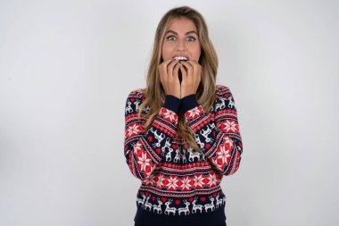 Dilsiz, sarışın, örgü örülü Noel süveteri giyen güzel bir kadın el ele tutuşup, ağzı açık bir şekilde kameraya şoke edici haberlere tepki veriyor.