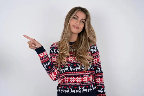 漂亮的金发女人穿着针织圣诞毛衣 站在空白的地方展示广告 人与晋升概念 — 图库照片