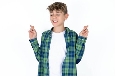 Beyaz arka plan üzerine ekose gömlek giyen yakışıklı genç çocuk umut ve gözler kapalı gülümseyerek el işareti yapıyor. Şans ve batıl inanç..