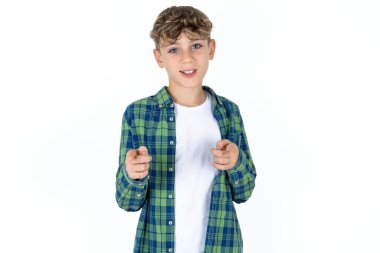Beyaz arka planda ekose gömlekli yakışıklı bir çocuk mutlu ve komik yüzlü parmaklarını kameraya doğrultuyor. İyi enerji ve titreşimler.