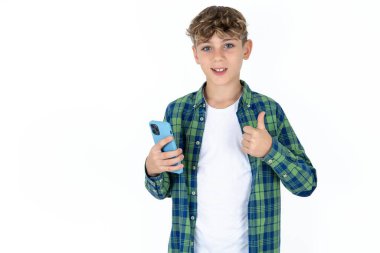 Beyaz arka planda ekose gömlekli yakışıklı bir gencin portresi akıllı telefonuyla mesajlaşıyor, gülüyor, gülümsüyor tamam işareti yapıyor, parmaklarıyla başparmağını kaldırıyor, mükemmel bir işaret.