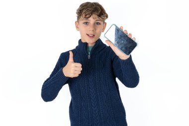 Mavi süveterli yakışıklı beyaz çocuk, hücresinde elinde siyah ekran başparmağını kaldırıyor.