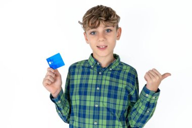 Beyaz arka planda ekose gömlek giyen yakışıklı genç çocuk kredi kartı noktasını boş tutuyor.