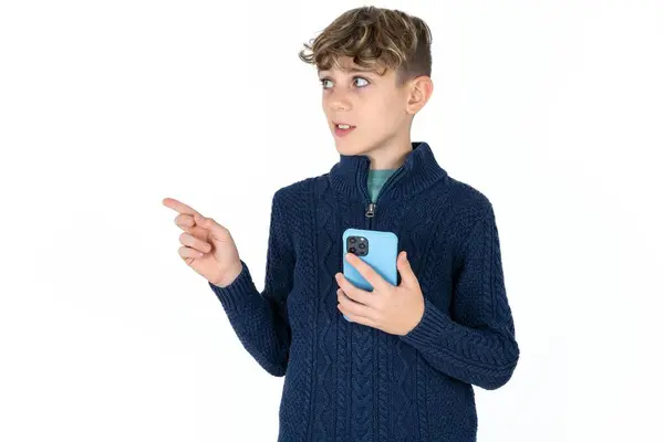 笑顔ハンサムコーカサス 青いセーターでティーン 男の子 携帯電話を保持し コピースペースを指す — ストック写真