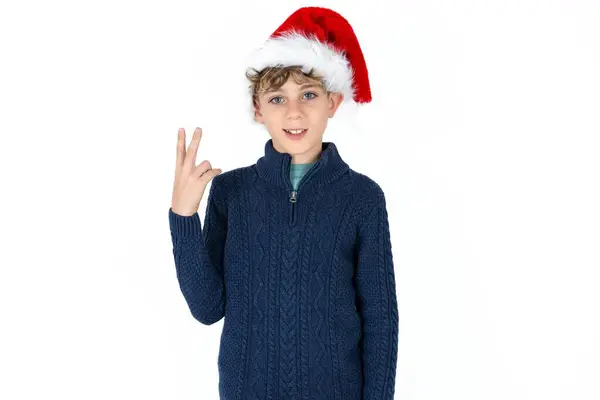 青いセーターとクリスマスのハット笑顔とフレンドリーに見えるハンサムな慎重な十代の少年は 数を数え下げて 手で2番目または2番目を示しています — ストック写真