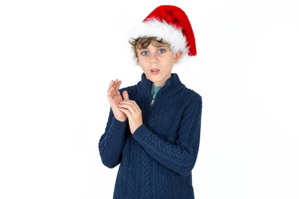 青いセーターとクリスマスの帽子で感情的なハンサムな慎重な十代の少年は 不信で手のひらをこすり カメラを見つめる — ストック写真