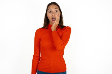 Beyaz arka plan üzerine kırmızı balıkçı yaka giyen genç İspanyol kadın çok şaşırmış görünüyor. Beklenmedik haberler karşısında afallamış ve şaşırmış görünüyor..