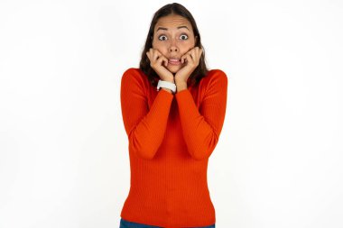 Beyaz arka plan üzerine kırmızı balıkçı yaka giyen, korkmuş ve korkmuş hisseden, korku ve korku dolu, kırmızı balıkçı yaka giyen genç bir kadın..