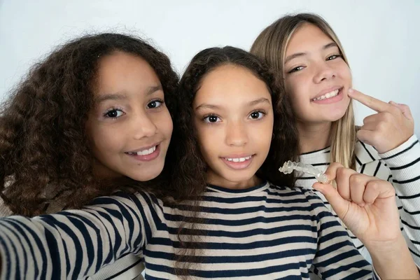Üç güzel, çok ırklı kız çocuğu görünmez bir diş teli ile selfie çekiyorlar ve bu yeni tedaviyi öneriyorlar. Diş sağlığı konsepti.