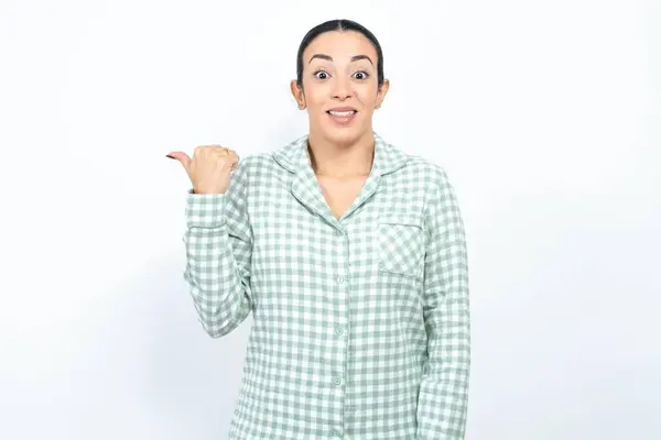 漂亮的年轻女子 身穿绿色格子布睡衣 背景洁白 食指指向一边 在复印版上显示有便宜货的消息 — 图库照片