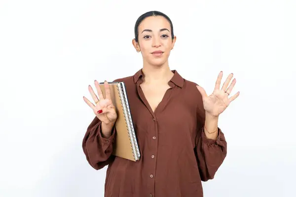美丽的女阿拉伯学生拿着印有纸的笔记本 用9号手指指尖 面带微笑 自信而快乐 — 图库照片