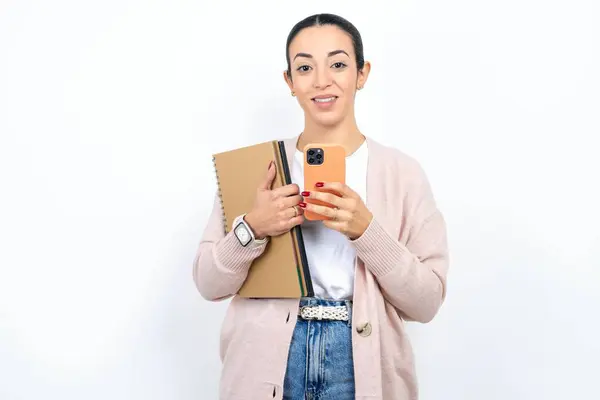 美丽的阿拉伯女学生背着笔记本在白色的背景上享受远距离的交流 使用手机 在网上冲浪 开心的笑着 在网上购物 — 图库照片
