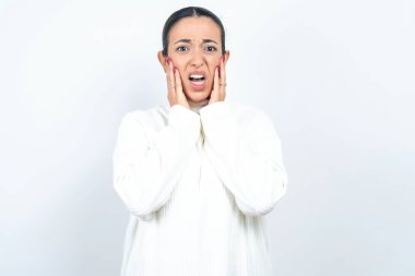 Üzgün, güzel bir Arap kadın beyaz arka planda poz veriyor. İki eliyle yüzüne dokunuyor.