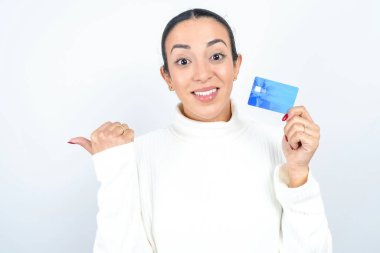 Beyaz arkaplanda poz veren güzel Arap kadın kredi kartı noktasını boş tutuyor