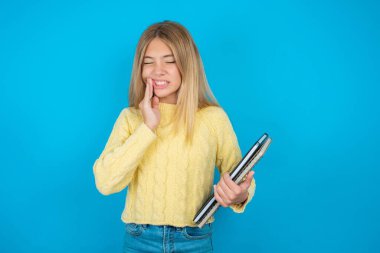 Sarı süveter giyen güzel bir kız diş ağrısı ya da diş hastalığından dolayı acı dolu bir ifadeyle ağıza dokunuyor..