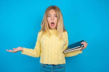 Hayal kırıklığına uğramış, sarı kazak giyen güzel kız şaşkın ve tereddütlü hissediyor, omuz silkiyor, ağzı açık, ne yapacağını bilmiyor..