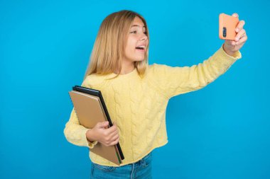 Sarı kazak giyen güzel bir kız. Sosyal medyaya göndermek için selfie çekiyor. Ya da arkadaşlarıyla video görüşmesi yapıyor..