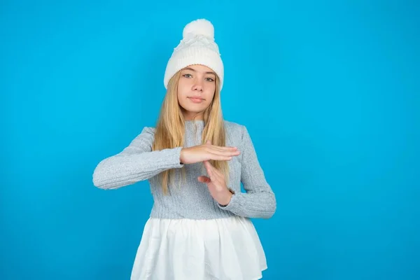 タイムアウトのジェスチャーを示す動揺している白い編まれた帽子と青いセーターを身に着けている美しい少女は 停止を必要とし ハードワークの後に休息のための時間を尋ねます — ストック写真