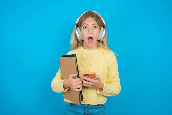 漂亮的小女孩穿着黄色的毛衣张开嘴拿着电话阅读广告难以置信的大购物价格 — 图库照片