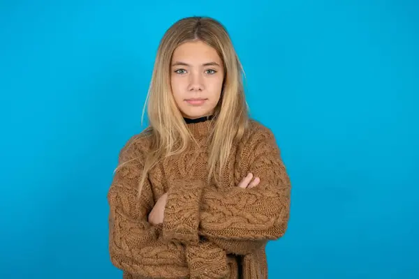 Self confident serious calm Beautiful kid girl wearing brown knitted sweater stands with arms folded. Shows professional vibe stands in assertive pose.