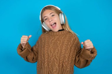 Duygusal güzel kız kahverengi örülü süveter giyen kız yüksek sesle bağırıyor. Kazanan elini kaldırıyor, yumruğunu sıkıyor, ağzı açık kulaklıklar takıyor. Evet jest yapıyor, en sevdiği müziği dinliyor.