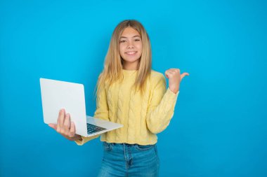 Sarı kazak giyen güzel bir kız boş yer tutuşu dizüstü bilgisayarı yönetiyor.