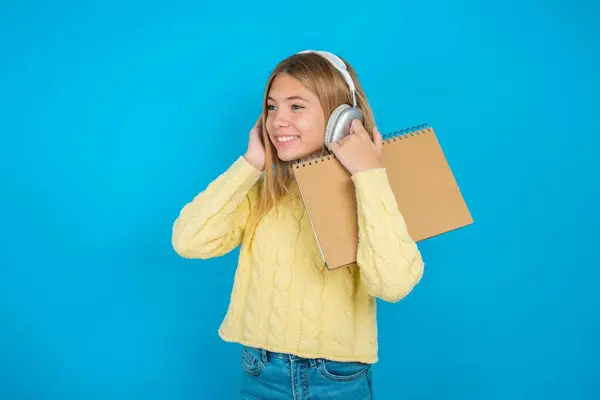 穿着黄色毛衣的漂亮小女孩戴着立体声耳机 聚精会神地听音乐 人们的业余爱好生活方式概念 — 图库照片