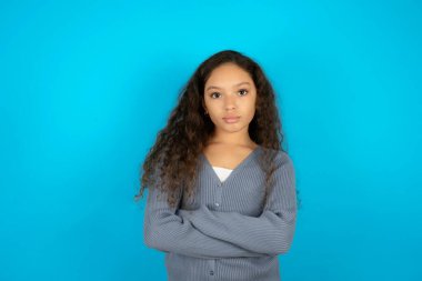 Ciddi ciddi düşünceli, mavi arka plan üzerine sıradan bir ceket giyen güzel bir kız çocuğu havalı, kendine güvenen girişimci çapraz elleri gibi hisseder..