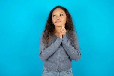 Çekici, neşeli, mavi arka plan üzerine gündelik ceket giyen güzel bir kız. El ele tutuşup bir fikir oluşturma planı yapıyor..