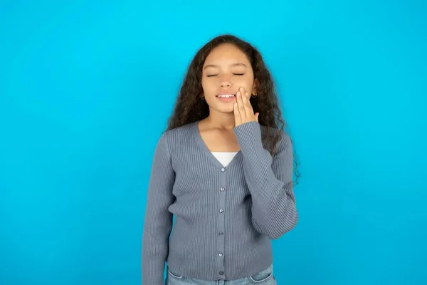 由于牙痛或牙病 漂亮的小女孩穿着休闲装 戴在蓝色背景下 手牵着嘴 脸上带着痛苦的表情 — 图库照片