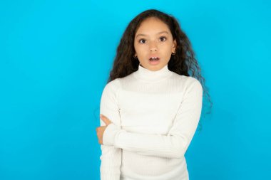 Utanmış, mavi arka plan üzerine beyaz balıkçı yaka giyen güzel kız ağzını açık tutuyor. İnanılmaz bir yenilik duyuyor sersemlemiş gibi bakıyor.