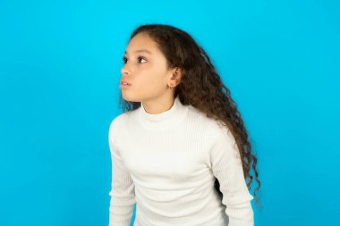 Mavi arka plan üzerine beyaz boğazlı kazak giyen güzel bir kız çocuğu şaşırmış ifadesini bir yana bırakınca nutku tutuluyor. Utangaç model şaşırmış görünüyor.