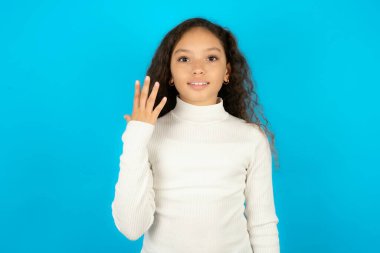 Mavi arka planda beyaz balıkçı yakalı güzel bir kız gülümsüyor ve arkadaş canlısı görünüyor, 5 ya da 5 numarayı gösteriyor, geriye doğru sayıyor.