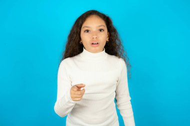 Şok olmuş, beyaz balıkçı yaka giyen güzel bir kız çocuğu mavi arka plan noktalarına sersemlemiş bir ifadeyle sana bakıyor.