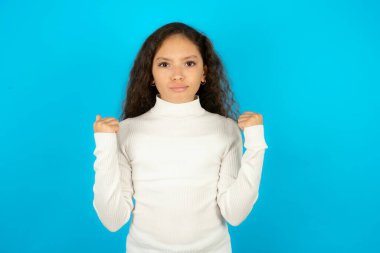 Mavi arka plan üzerine beyaz boğazlı kazak giyen sinirli, güzel bir kız çocuğu. Öfkeyle yanaklarına vuruyor ve yumruklarını kaldırıyor. Öfke ve agresif duyguları ifade ediyor. Öfkeli model
