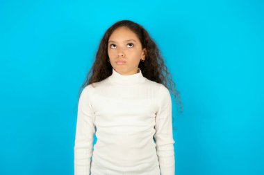 Tatminsiz bir kız çocuğu mavi çantaların üzerine beyaz boğazlı kazak giyiyor ve mutsuz bir ifade takınıyor gücenmiş duruyor. Bunalımlı model.