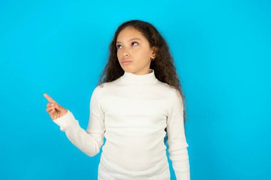 Güzel bir kız çocuğu mavi arka plan noktalarında beyaz balıkçı yaka giyiyor ve reklam yapıyor. En iyi fiyat öneriyor..