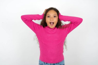 Neşeli, neşeli, pembe balıkçı yaka giyen güzel bir kız çocuğu beyaz arka plan tepkisi veriyor. Harika haberler aldıktan sonra ellerini havaya kaldırıyor..