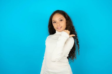 Beyaz balıkçı yaka kazak giyen etkileyici bir kız çocuğu. Arka planda mavi nokta boş alan.