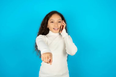 Mavi arka planda beyaz boğazlı kazak giyen güzel bir kız çocuğu kameraya doğrudan bakıyor telefon konuşmaları uzun saatler konuşmaktan keyif alıyor. Bana katıl.