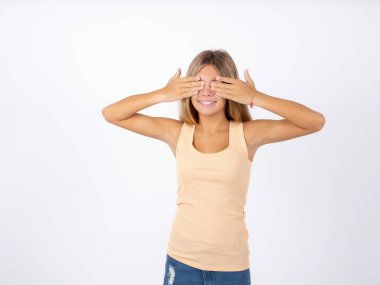 Beyaz stüdyo arka planında kolsuz tişört giyen genç bir kız. Gözleri neşeli ve komik gülümseyerek kapatıyor. Kör kavram.