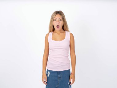 Oh my God. Surprised teen girl wearing sleeveless t-shirt over white studio background stares at camera with shocked expression exclaims with unexpectedness, clipart