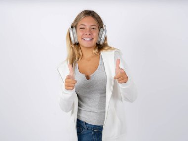 teen girl with headphones wearing white jacket over white studio background directs fingers at camera selects someone. I recommend you. Best choice clipart