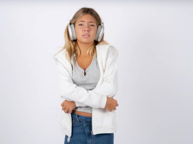 teen girl with headphones wearing white jacket over white studio background shaking and freezing for winter cold with sad and shock expression on face. clipart