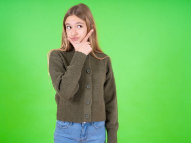 Güzel beyaz kız yeşil kazak giyiyor. Bir soru hakkında endişeleniyor. Endişeli ve gergin..