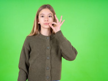 Yeşil kazak giyen güzel beyaz bir kız ağzı ve parmaklarıyla fermuar gibi kapalı dudakları var. Gizli ve sessiz, tabu konuşması.