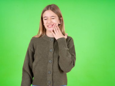 Yeşil kazak giyen güzel beyaz kız diş ağrısı ya da diş hastalığından dolayı acı dolu bir ifadeyle dudaklarına dokunuyor..