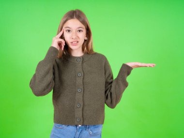 Güzel beyaz kız yeşil kazak giyiyor. Kafası karışmış ve avuç içi açık, fotokopi alanı gösteren ve alnını işaret eden birinden rahatsız olmuş. Bunu bir düşün..