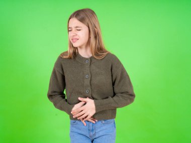 Güzel beyaz kız yeşil kazak ve eli karnında kot pantolon giyiyor çünkü mide bulantısı, acı verici bir hastalık kendini iyi hissetmiyor. Ache kavramı.