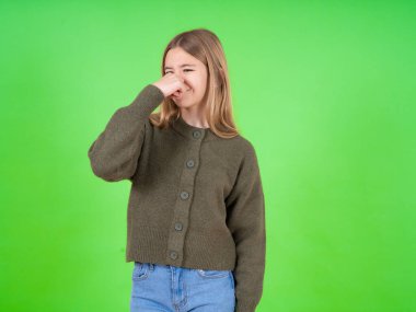 Güzel beyaz kız yeşil kazak ve kot pantolon giyiyor. Kokuşmuş ve iğrenç bir koku alıyor. Dayanılmaz bir koku. Kötü kokuyor.